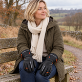Woman with a blonde bob wearing WASOTO WG002 heated gloves, seated on a countryside bench with both gloved hands resting naturally on her thighs.